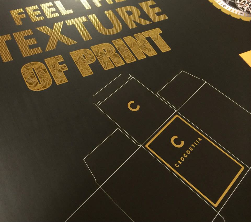 Black print sample showcasing gold foil text and tactile raised-varnish grid layout promoting textured print