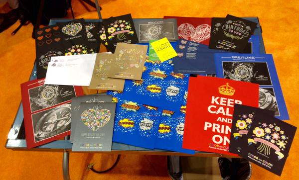 Colorful display of printed samples featuring metallic foil, embossing, and decorative print effects on a table.